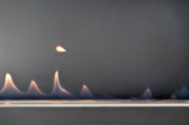 Metal ocakta mavi gaz alevleri, stüdyo kapanışı havada asılı duran küçük damlacık ateşleme, minimalist endüstriyel durum, güvenlik teknisyeni test pilotu