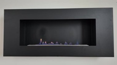 Dans eden alevlerle donatılmış şömine, siyah çerçeve çizgisel etanol yakıcı, mavi ve turuncu alevler çakıl taşları arasında titreşiyor, ruh hali yaratıyor.