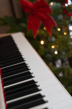 Noel piyanosu anahtarları, Noel ağacı, siyah beyaz anahtarlar, bulanık bokeh ışıkları ve kırmızı pruva, rahat oturma odası havası, piyanist hazırlanıyor.