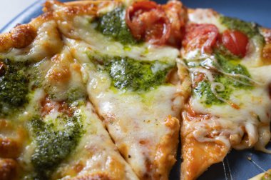 Yakından eritilmiş peynirli pizza dilimi, pesto ve vişneli domates sosu, yapışkan mozzarella iplikleri, mavi tabakta altın kabarcık, sıcak ev tarzı ışıklandırma.,