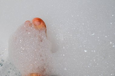 Ayak parmakları yoğun beyaz köpükten bakıyor, serbest tasarımcı işten sonra gevşiyor, sıcak banyo suyu, hafif ışıklandırma, sakin atmosfer, ince cilt detayı