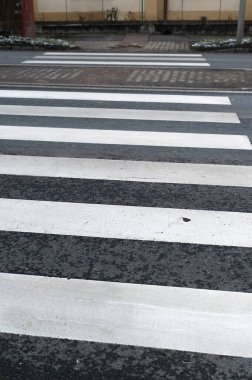 Zebra asfaltta kaldırım kenarından geçiyor, tramvay rayları ve hafif kar bantları olan boş bir cadde, beyaz boya şeritleri, bulutlu aydınlatma, kapalı lowangle