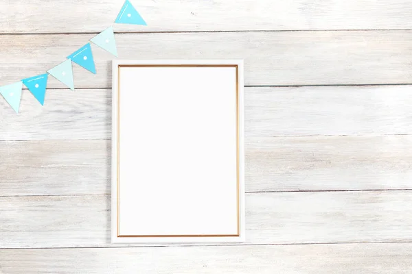 A white and gold photo frame lies on a plank table with blue flags. Festive photo frame mockup.