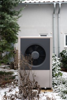 Modern hava kaynağı ısı pompası üniteleri yerleşim yerinin dışına kurulmuş. Fotoğraf, kuru bitkiler ve karla çevrili enerji verimli ısıtma sistemlerini gösteriyor. Soğuk iklim için sürdürülebilir ev çözümleri gösteriyor.