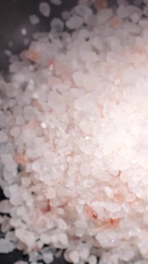 Yakın plan çekimde kaba tuz kristalleri bir kaseye dökülürken ışığı yansıtıyor. Doku ve ışıltı yemek pişirme sürecine bir göz atmamızı sağlıyor..