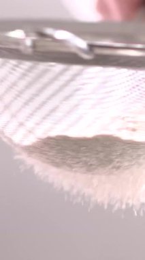 Güneşli bir mutfakta, bir el ince bir süzgeçten unu nazikçe geçirir. Sahne, taze pişmiş ekmek malzemelerini hazırlarken alınan hassasiyeti ve özeni yakalıyor..