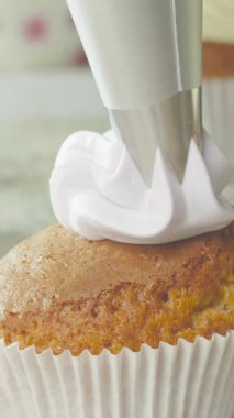 Parlak bir mutfakta yeni pişmiş keklerin üzerine ustalıkla tüy gibi yumuşak borular döşeyen bir fırıncı. Her kek, güzel tasarımları olan lezzetli bir ziyafete dönüşüyor..