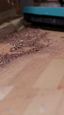 Bir kişi atölyede ahşap bir yüzeyi temizlemekle meşgul. Düzenli bir çalışma alanını korumak için toz ve odun talaşları temizleniyor. Süreç ayrıntılara ve özene dikkat eder.