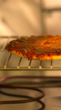 Fırından yeni çıkmış bir pizza altın kabuğunu ve erimiş peynirini sergiliyor. Aroma, askı soğudukça mutfağı doldurur..