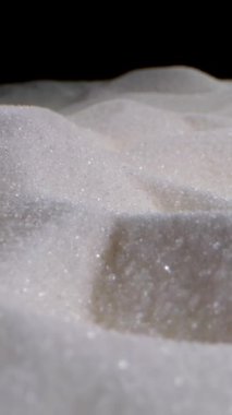 Yakın çekim beyaz granüllü şeker, pürüzsüz kaydırma hareketi. Köpüklü şeker kristalleri yiyecek, tatlı veya arka plan kullanımı için mükemmel soyut bir doku oluşturur..