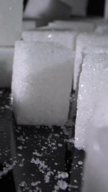 Şeker küpleri, parlak dokularını gösteren siyah bir yüzeyde düzgünce düzenlenir. Etrafı şekerle çevrili. Kurulumun tatlılığını ve temizliğini vurguluyor..