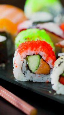 Taze balık ve sebzelerden oluşan renkli suşi rulolarının yakın çekimi, siyah bir tabakta güzelce sıralanmış. Suşi severler için mükemmel. Bir sonraki yemek için görsel ilham arıyorlar..