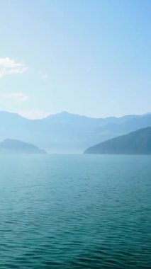 Sakin su, sabah sisi dağların üzerinde süzülürken yumuşak ışığı yansıtır. Doğa güzelliğini göl kenarındaki huzurlu bir arazide gösterir..