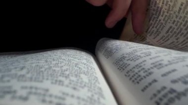 Bir el, metinle dolu bir kitabın sayfalarını nazikçe çevirir. Atmosfer sakin ve loş ışık okumak için rahat bir ortam yaratıyor..