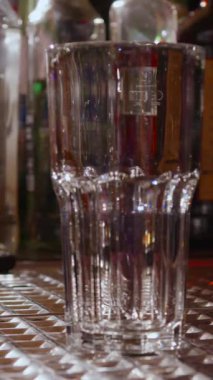 Barmenin bardağa buz attığı yakın plan bir fotoğraf. Bardağı doldururken berrak buz şıngırdar ve ferahlatıcı bir kokteyl hazırlar. Miksoloji videoları ve içecek için mükemmel bir görüntü.