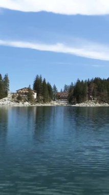 Sakin sular, gölü çevreleyen ağaçların berrak mavi gökyüzünü ve sahilde huzur içinde bir kulübeyi yansıtıyor. Rahatlamak ve doğanın tadını çıkarmak için mükemmel bir gün..