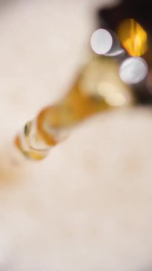 Yağ dikkatlice şişeden temiz bir konteynıra dökülüyor. Mutfak iyi aydınlatılmış, yağın zengin rengini ve hareketlerini gösteriyor..