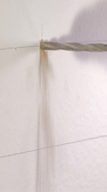 Bir kişi, duvarda tesisat için bir delik açmak için matkap kullanıyor. Ayarlar bir ev gibi görünüyor, ve kişi odaklanmış ve dikkatli, matkabın hassasiyetini sağlıyor..