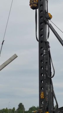 Bir inşaat ekibi inşaat alanında büyük bir beton kirişi kaldırmak için ağır makineler kullanır. Gökyüzü bulutlu, potansiyel yağmuru gösteriyor.