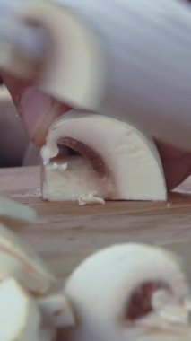 Ev mutfağında taze beyaz mantar doğramak, yaklaşan yemeğin hazırlanmasını ön plana çıkarıyor. Basit pişirme teknikleri taze malzemelerle sergilenir..