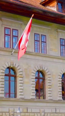 İsviçre 'de aydınlık bir günde zarif bir tarihi binanın önünde bayrak sallanıyor. İnsanlar rahatça dolaşır, güzel atmosfer ve mimarinin tadını çıkarırlar..