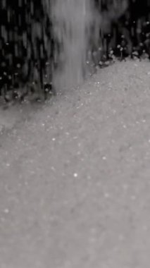 Yukarıdan düşen şeker tanelerinin yavaş çekim videosu yumuşak, ışıl ışıl bir yüzey oluşturuyor. Saniyede bin kare çekilen sahne, bireysel hareketin dokusunu ve güzelliğini vurgular.