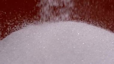 Yukarıdan düşen şeker tanelerinin yavaş çekim videosu yumuşak, ışıl ışıl bir yüzey oluşturuyor. Saniyede bin kare çekilen sahne, bireysel hareketin dokusunu ve güzelliğini vurgular.