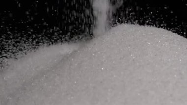 Yukarıdan düşen şeker tanelerinin yavaş çekim videosu yumuşak, ışıl ışıl bir yüzey oluşturuyor. Saniyede bin kare çekilen sahne, bireysel hareketin dokusunu ve güzelliğini vurgular.