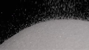 Yukarıdan düşen şeker tanelerinin yavaş çekim videosu yumuşak, ışıl ışıl bir yüzey oluşturuyor. Saniyede bin kare çekilen sahne, bireysel hareketin dokusunu ve güzelliğini vurgular.