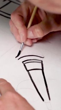 Bir sanatçı, boş bir tuval üzerinde düzgün ve hassas çizgiler yaratmak için ustaca küçük bir fırça kullanır. Parlak stüdyo ışığı işin karmaşık detaylarını ve odaklanmasını vurguluyor..