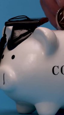 Bir el, mezuniyet şapkasıyla tasarlanmış bir domuz kumbarasına bozuk para koyar. Bu sahne eğitim ve öğrenciler için finansal planlamanın önemini vurgular..