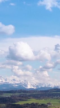 Bulutlar, parlak mavi gökyüzünün altındaki büyüleyici kar örtülü dağların üzerinde tembelce sürükleniyor. Bu huzurlu ortam doğanın gündüz güzelliğini gözler önüne seriyor..