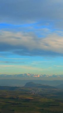 Dağlar, vadinin üzerinde bulutlar sürüklenirken gün doğumuyla yavaşça parlar. Bu huzurlu sahne doğanın güzelliğini ve sabahın sükunetini yakalar..