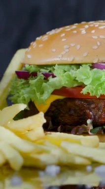 Marul, domates ve peynirle kaplı taze yapılmış hamburger ve yanında da tabakta kızarmış patates. Tadını çıkarmaya hazır lezzetli bir yemek.