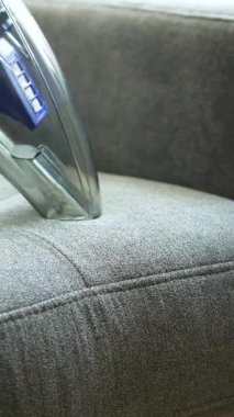 Bir el temizleyicisi gri döşemeli bir sandalyede toprak ve lekeleri temizlemek için kullanılıyor. Bu süreç ev eşyaları için etkili temizlik teknikleri sergiliyor.