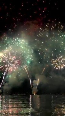 Huzurlu bir gölün üzerinde parlak renkler halinde parlak havai fişekler patlıyor. Suya çok güzel yansıyor. Canlı görüntü, gece gökyüzünün altında şenlikli bir atmosfer yaratıyor..