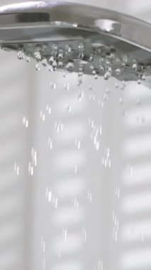 Duş başlığından akan sular rahatlatıcı bir atmosfer yaratıyor. Güneş ışığı, sakin bir banyodaki sabah rutininin canlandırıcı deneyimini arttırır..