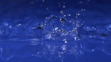 Yağmur damlaları pürüzsüz mavi bir yüzeye düşer ve güzel dalgalanmalar yaratır. Huzurlu sahne, su ışık ve renkle etkileşime girerken doğanın güzelliğini gösteriyor..