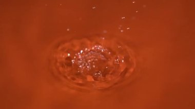 Canlı turuncu sıvının içine sıçrayan damlacıklar büyüleyici dalgalanmalar yaratır. Işık ve suyun etkileşimi çarpıcı bir görsel deneyim sunuyor..