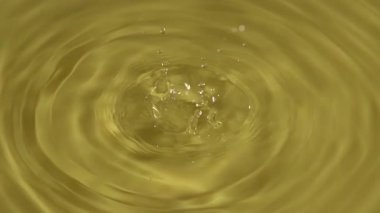 Yakından bakınca, sanatsal efekt için parlak ışıkta parlak dalgalar ve yansımalar yaratan altın sıvıdan oluşan bir havuza bir damla su sıçrıyor..