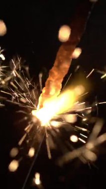 Parıltılı kıvılcımlar saçan, karanlık bir ortamda parlayan bir maytap. Arkadaşlar toplanır, kutlama sırasında gülümseme ve heyecanla anın tadını çıkarırlar..