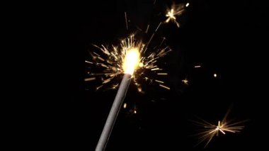 Bir havai fişek, arka bahçede gece parlayan kıvılcımlar gösteriyor. İnsanlar bu sevinç anını izlemek ve tadını çıkarmak için toplanıyor. Gece gökyüzü ekran renkleriyle parlıyor..