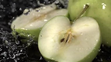 Yeşil elma dilimleri siyah bir yüzeye yerleştirilir. Elmalar kesildiğinde su etrafa sıçrıyor, parlak ve taze bir görüntü sergiliyor..