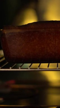 Bir şefin sıcak fırından yeni çıkmış bir keki dikkatlice çekerken yakın plan çekimi. Sıcak ışıklandırma, profesyonel bir mutfağın altın kabuğunu ve rahat atmosferini ön plana çıkarıyor. Bu görüntü için ideal.