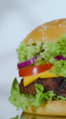 Hamburger, taze sebze, peynir ve köfte katmanlarından yapılır. Tahta üzerinde gösteriliyor. Hamburgerin renkleri göze çarpıyor..