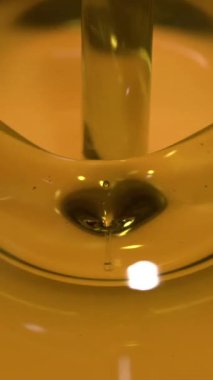 Pürüzsüz bir altın zeytinyağı akıntısı, saniyede 1000 karelik detaylı bir ağır çekimde yakalanan cam bir kaba nazikçe akar. Sıvı yumuşak yansımalar yaratır ve zengin sıcak tonlarda vurgu yapar.