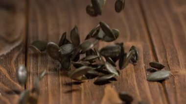 Balkabağı tohumları yakın plan çekimde ahşap bir masaya düşer. Işık tohumların dokusunu ve ahşabın yüzeyini vurgular. Bu an, tohumların yere inerken ki hareketlerini yakalar..