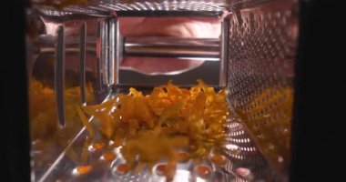 Öğütülmüş sarı peynir metal rendesinin dibinde birikir. Eller mutfak ortamında yemek için peynir hazırlarken görülüyor..