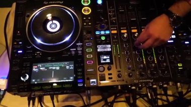Bir DJ yerel bir etkinlikte farklı müzik parçalarını karıştırmak için profesyonel ekipman kullanır. Kalabalık neşeli atmosferin keyfini çıkarırken DJ sesi kontrol ediyor..