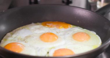 Yumurtalar kızartma tavasına konur, sıcaktan pişer. Tuz ve karabiber lezzet için eklenir. Bu, mutfakta yaygın bir kahvaltı hazırlama sürecini gösterir..